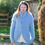 Une femme portant une confortable Veste en mohair de chevreau Vannerie tricotée à la main bleue, debout à l'extérieur par une journée ensoleillée.
