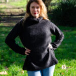 Femme confiante posant à l'extérieur dans un pull et un jean Pull Mousse col boule taille unique en kid-mohair et soie naturelle noirs, avec un fond naturel lumineux.