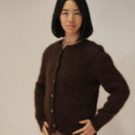 Une femme avec un sourire content portant une confortable veste boutonnée marron en pur mohair de chevreau Eternelle, debout sur un fond neutre.