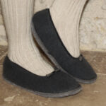 Cosy à la maison : une paire de pieds bien enveloppés dans des Ballerines en laine et mohair et de confortables chaussons gris foncé sur un fond rustique.