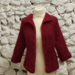Un cardigan confortable tricoté à la main bordeaux affiché sur un mannequin sur un fond blanc texturé.